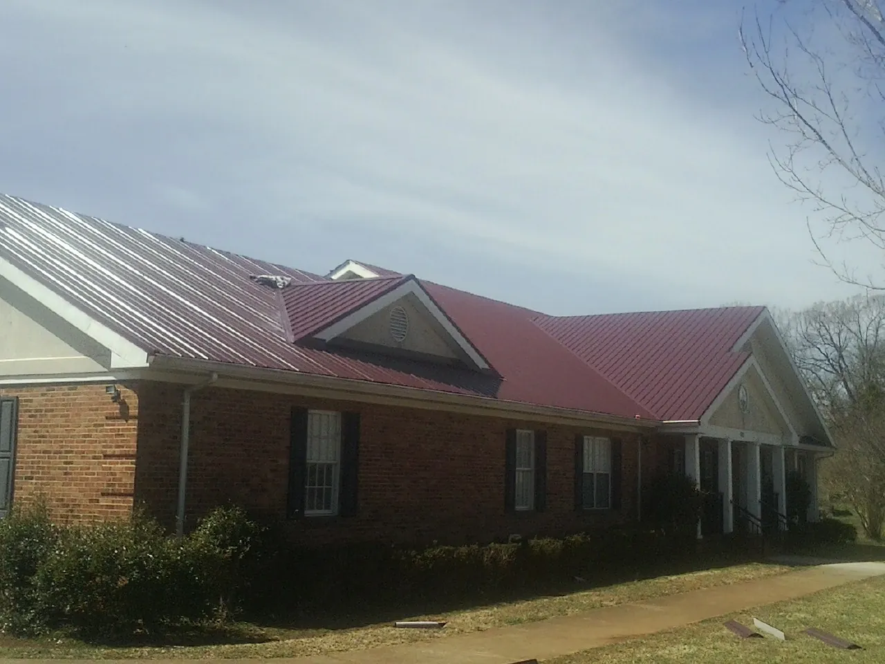 Red metal roof with gabled entries on a long brick building, from a Hail Damage Roof Repair job in Bakerstown