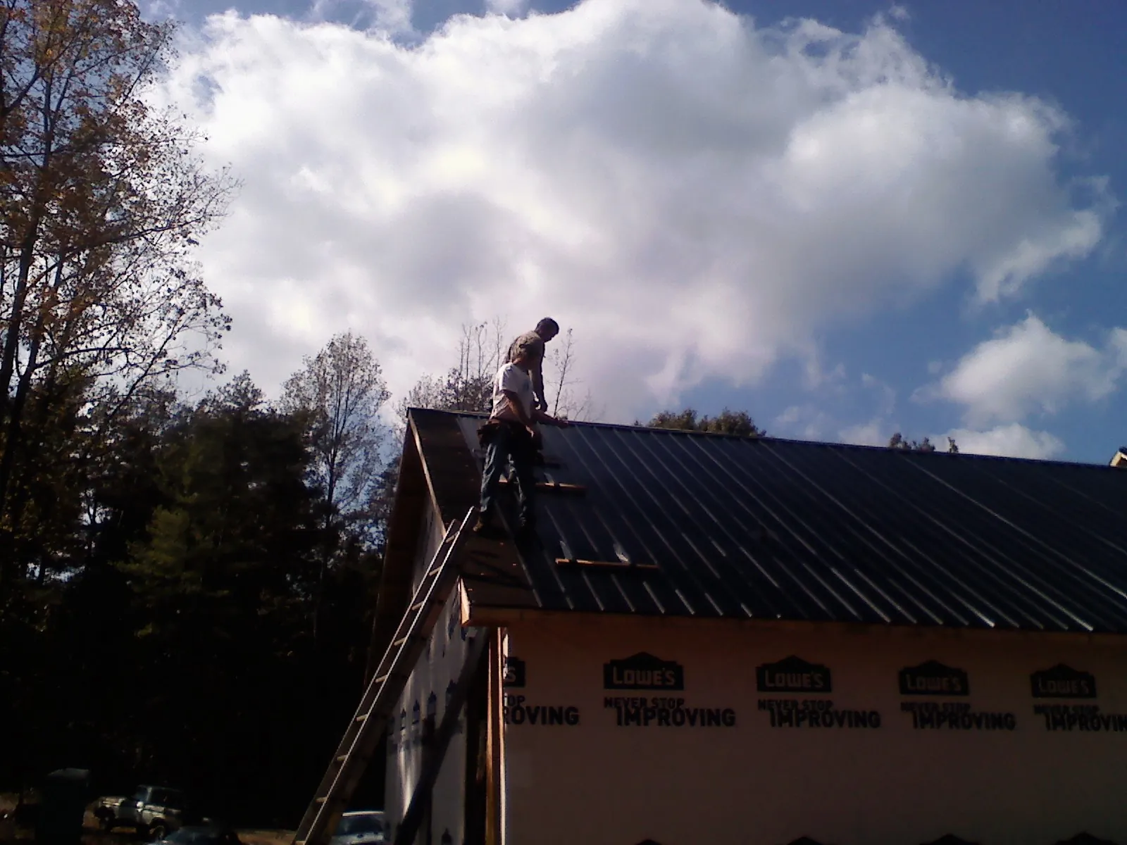 Roofer fastening dark metal panels high against a cloudy sky, from a Roof Inspection job in Bakerstown
