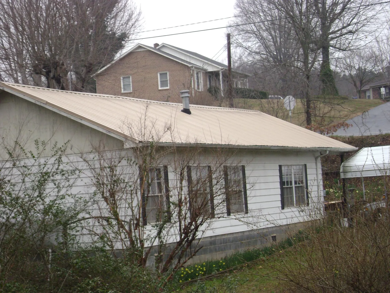 Tan metal roof on a white sided house set into a hillside — Commercial Roofing by Roofing Brothers in Bakerstown